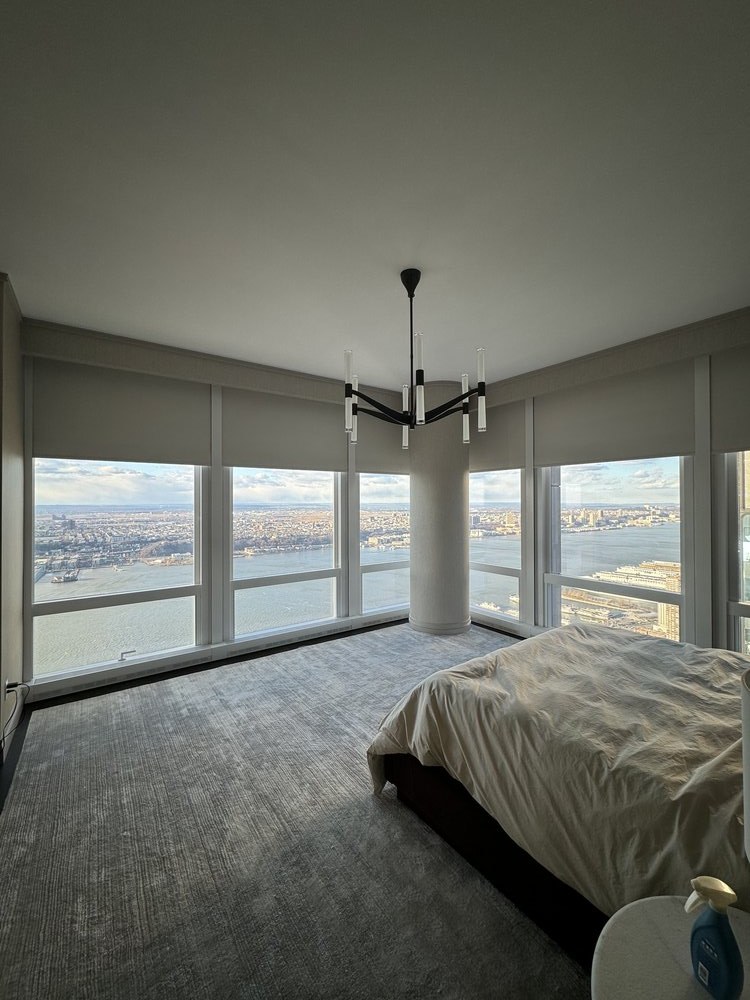 High-rise residential bedroom with expansive floor-to-ceiling windows showcasing panoramic city views. The